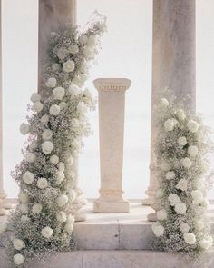 white flowers and greenery are arranged on pillars