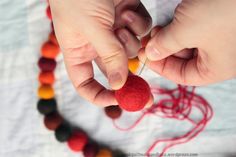 a person is making a bead necklace with red thread and orange beads on a white tablecloth