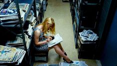 a woman sitting on a chair reading a book in a library filled with books and magazines