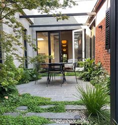 an outdoor dining area with chairs and table surrounded by greenery in front of a brick building