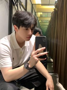 a young man sitting on the floor looking at his cell phone while wearing a white shirt and black pants