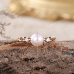 a white pearl and diamond ring sitting on top of a piece of wood with flowers in the background