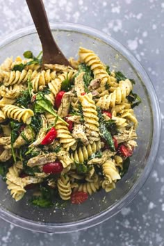 a pasta salad with chicken, spinach and tomatoes in a glass bowl on a table