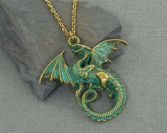 Dragon necklaces features a brass dragon with outstretched wings and verdigris green patina. Pendant is 1 11/16 inches tall, 1 13/16 inches wide (43 x 46mm). Gold plated chain - 18, 24 or 30 inches long. Find more women's necklaces here - https://www.etsy.com/shop/CharleneSevier?ref=hdr_shop_menu&section_id=10084290 Find more men's jewelry here - https://www.etsy.com/shop/CharleneSevier?ref=hdr_shop_menu&section_id=10866473 Enter my shop here - https://www.etsy.com/shop/CharleneSevier?re Fantasy Dragon Design Necklace, Gold Fantasy Style Necklace For Fantasy Events, Gold Fantasy Necklace With Dragon Design, Gold Fantasy Jewelry With Dragon Design, Gold Fantasy Dragon Necklace, Fantasy Gold Jewelry With Dragon Design, Unique Dragon Design Necklace Collectible, Unique Dragon Design Necklace For Collectors, Vintage Dragon Design Jewelry For Gifts