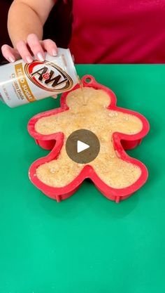 a person pouring milk on top of a cookie shaped like a gingerbread man with a can