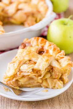 a slice of apple pie on a white plate with a fork next to the pie