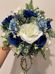 a bridal bouquet with blue and white flowers is held by a woman's hand