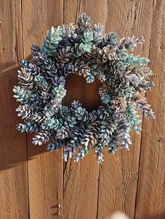 a wreath made out of pine cones on top of a wooden fence with someone's hand reaching for it