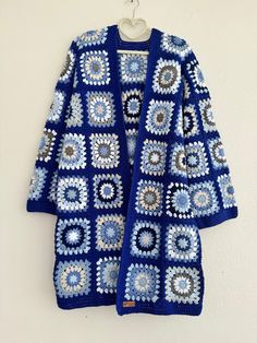 a blue crocheted cardigan hanging on a wall with a white hanger