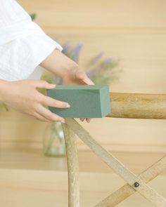 a person holding a block of wood on top of a wooden chair