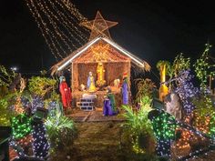 a nativity scene is lit up at night with lights on the roof and decorations around it