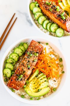 two white bowls filled with rice, salmon and cucumbers next to chopsticks