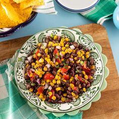 a bowl filled with black beans and corn next to tortilla chips on a cutting board