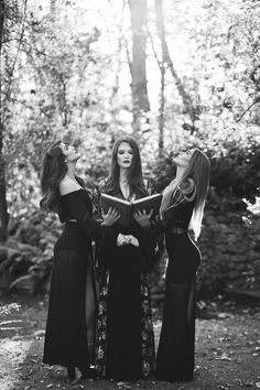 three women standing in the woods reading a book