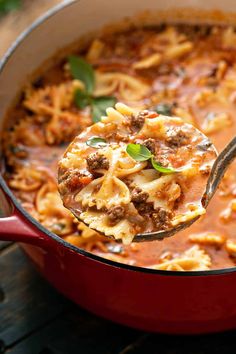 a ladle full of pasta and meat sauce being held by a spoon over a red pot