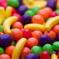 many different colored candy candies in a pile together with bananas and other fruits on top