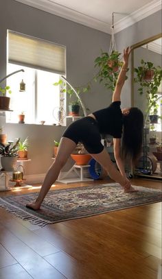 a woman is doing yoga in the middle of a room with potted plants on the wall