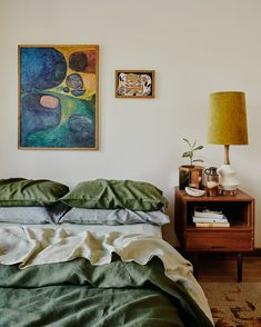 a bed with green sheets and pillows next to a painting on the wall above it