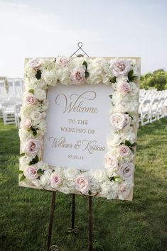 a welcome sign with white and pink flowers in front of an outdoor wedding ceremony venue