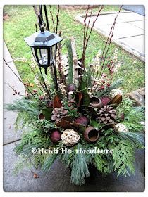 a vase filled with lots of flowers and greenery next to a lamp post on the sidewalk