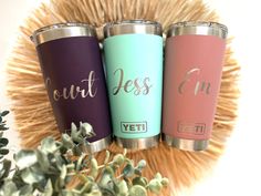 three personalized yeti tumblers sitting next to each other on top of a plant