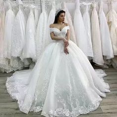 a woman in a white wedding dress sitting on the floor next to racks of dresses