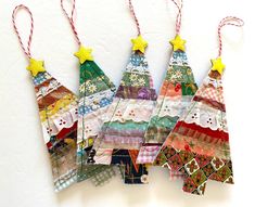 four small christmas trees are hanging from twine strings on the wall, decorated with colorful fabric