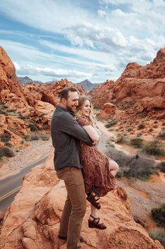 a man and woman standing on top of a rock formation in the middle of desert