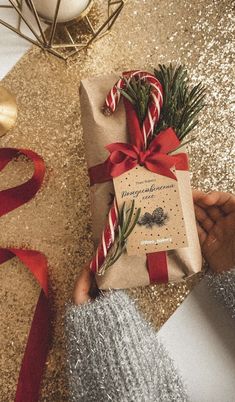 a person holding a wrapped present on top of a table next to a christmas tree