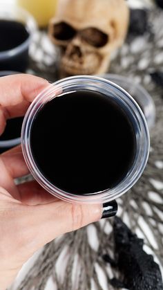 a hand holding a cup of black liquid on top of a table with skulls in the background