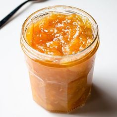 a glass jar filled with orange marmalade sitting on top of a white table