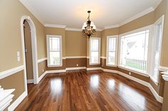 an empty living room with hard wood flooring and chandelier hanging from the ceiling