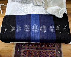 a bed with a blue and black blanket on top of it next to a rug