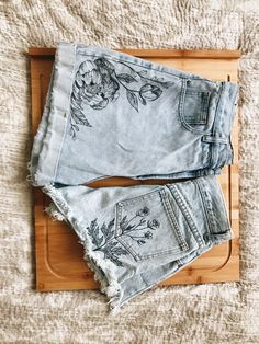 an old pair of jean shorts with flowers on them sitting on a wooden cutting board