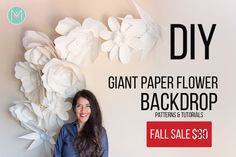 a woman standing in front of a wall with paper flowers on it and smiling at the camera