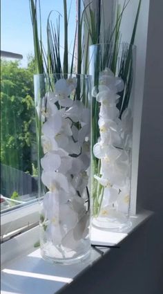 two clear vases filled with white flowers sitting on a window sill next to each other