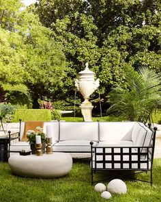 a white couch sitting on top of a lush green field next to a garden filled with lots of trees