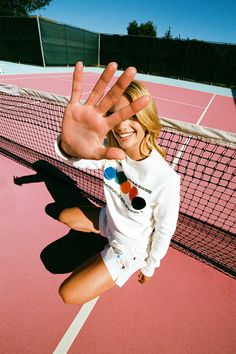 a woman standing on top of a tennis court holding her hand up