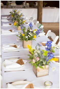 a long table is set with white linens and flower centerpieces for the tables