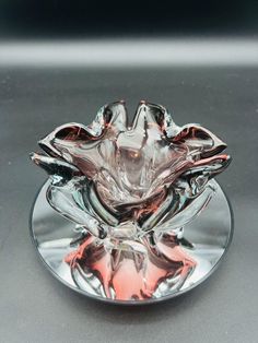 a clear glass bowl sitting on top of a silver plate with an orange flower in the center