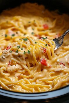 a close up of a fork in a bowl of pasta with chicken and cheese on it