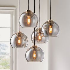 five clear glass globe pendant lights hanging from a ceiling fixture in a room with white walls and windows