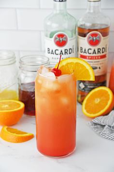 an orange drink with a cherry garnish on the rim next to bottles of alcohol