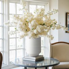 a vase with white flowers sitting on top of a table in front of a window