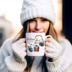 a woman is holding a coffee mug in her hands while wearing a hat and gloves