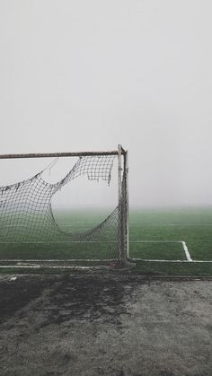 a soccer goal in the middle of a field on a foggy, overcast day