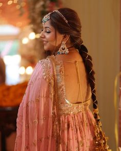 a woman in a pink dress with gold jewelry on her neck and back, looking off to the side