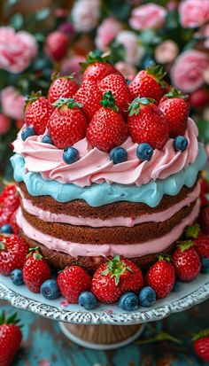 a cake with frosting, strawberries and blueberries on top sitting on a plate