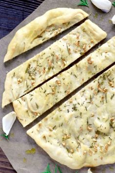 an uncooked pizza sitting on top of a table next to garlic and herbs