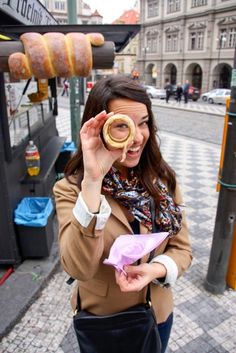 a woman holding up a doughnut in front of her eye while standing on the street